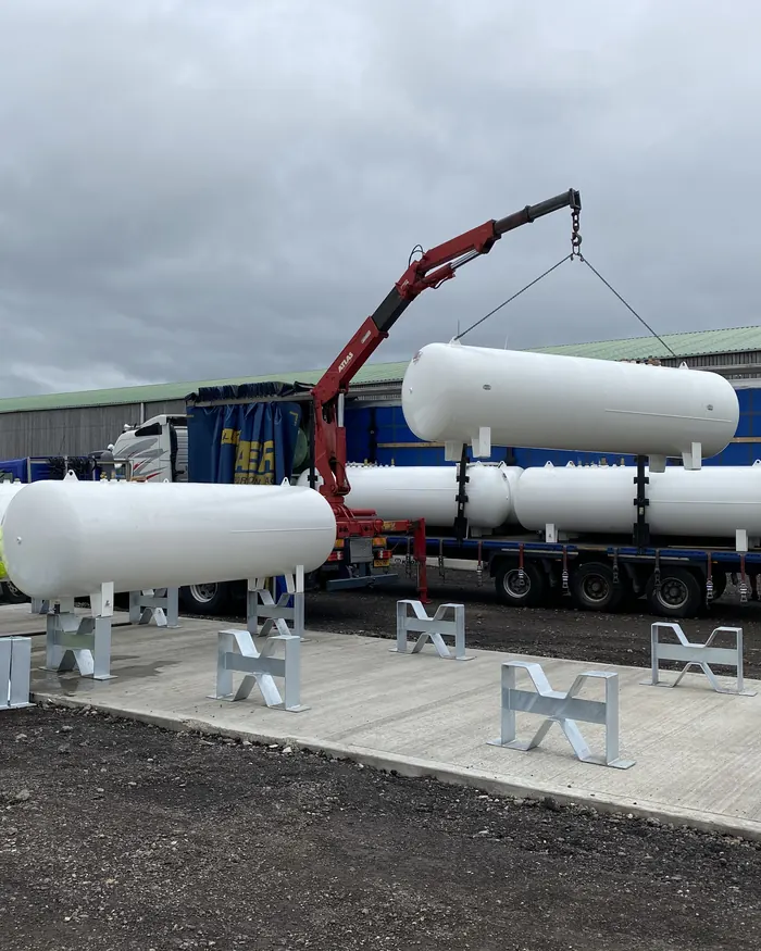 A lorry-mounted crane lifting bulk LPG tanks into position on a construction site