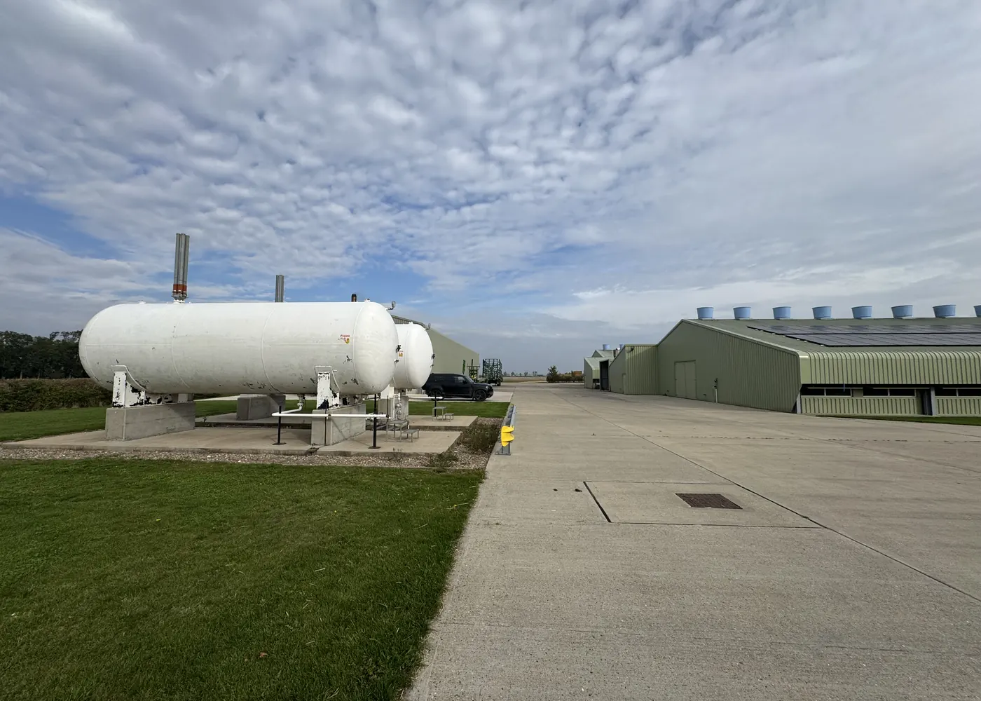 Two white above-ground LPG storage tanks on a concrete base beside a farm access road