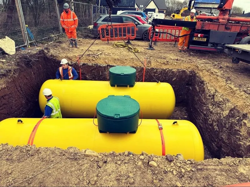 Two yellow underground LPG tanks being installed in an excavated pit by engineers