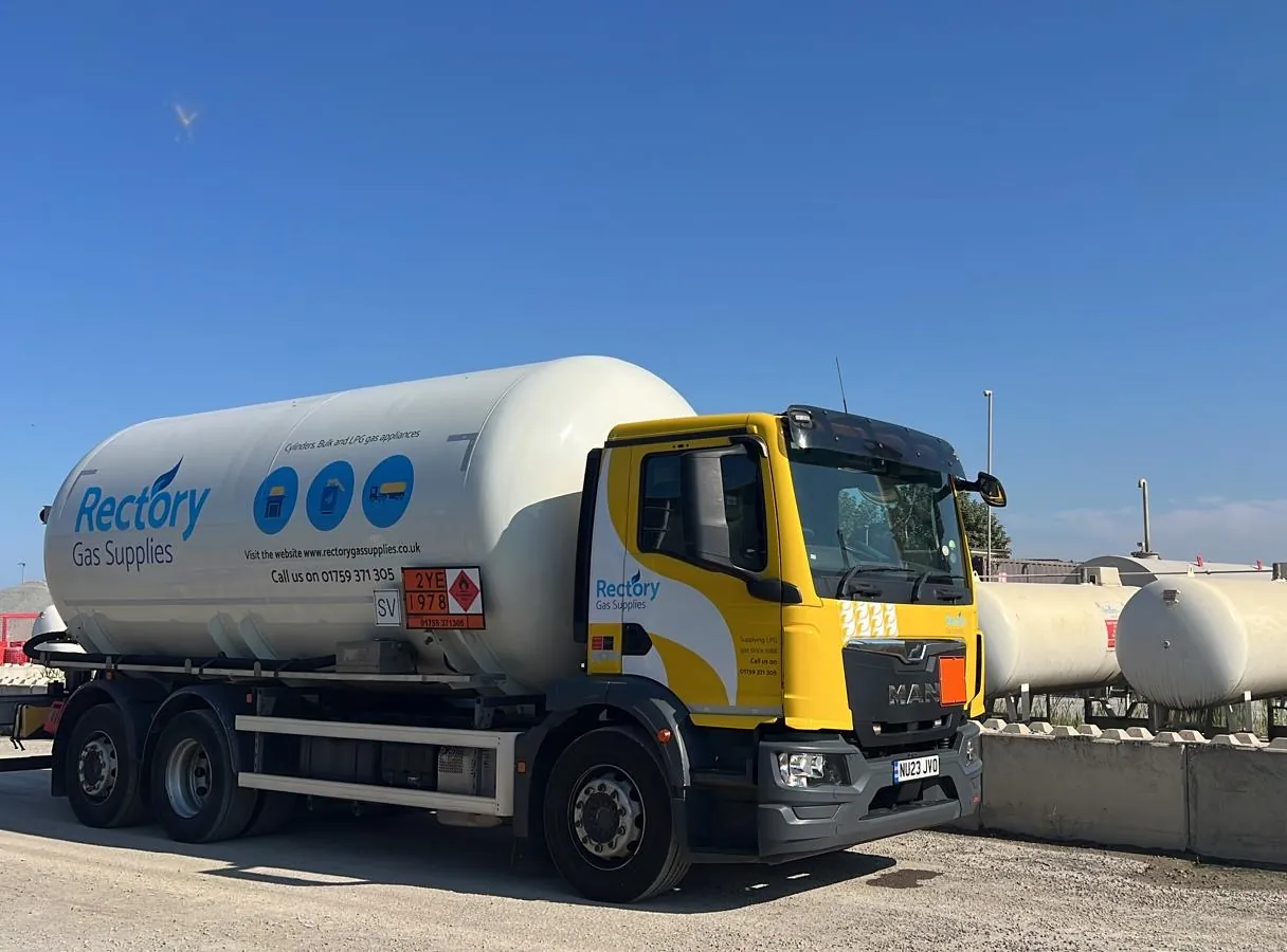 A yellow-cabbed Rectory Gas Supplies LPG tanker parked beside above-ground storage tanks at an industrial site