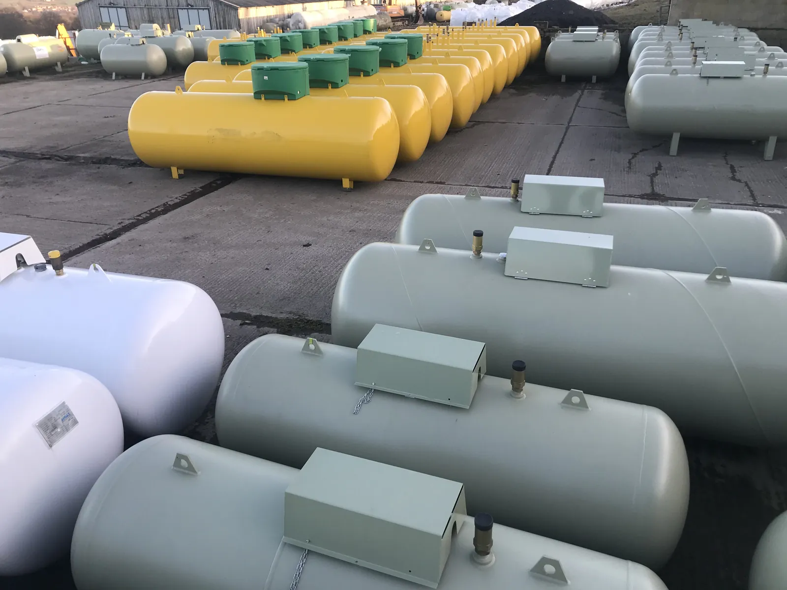 Rows of yellow and cream LPG storage tanks with green covers lined up in a tank yard
